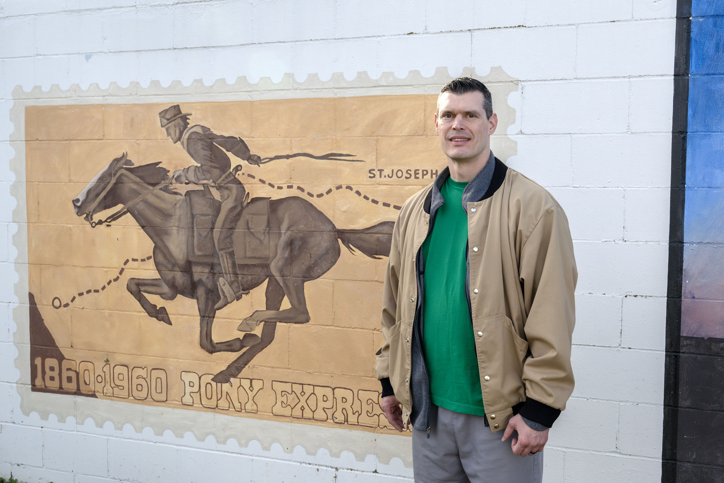 Jason Booth stands in front of his mural depicting a postage stamp honoring the Pony Express
