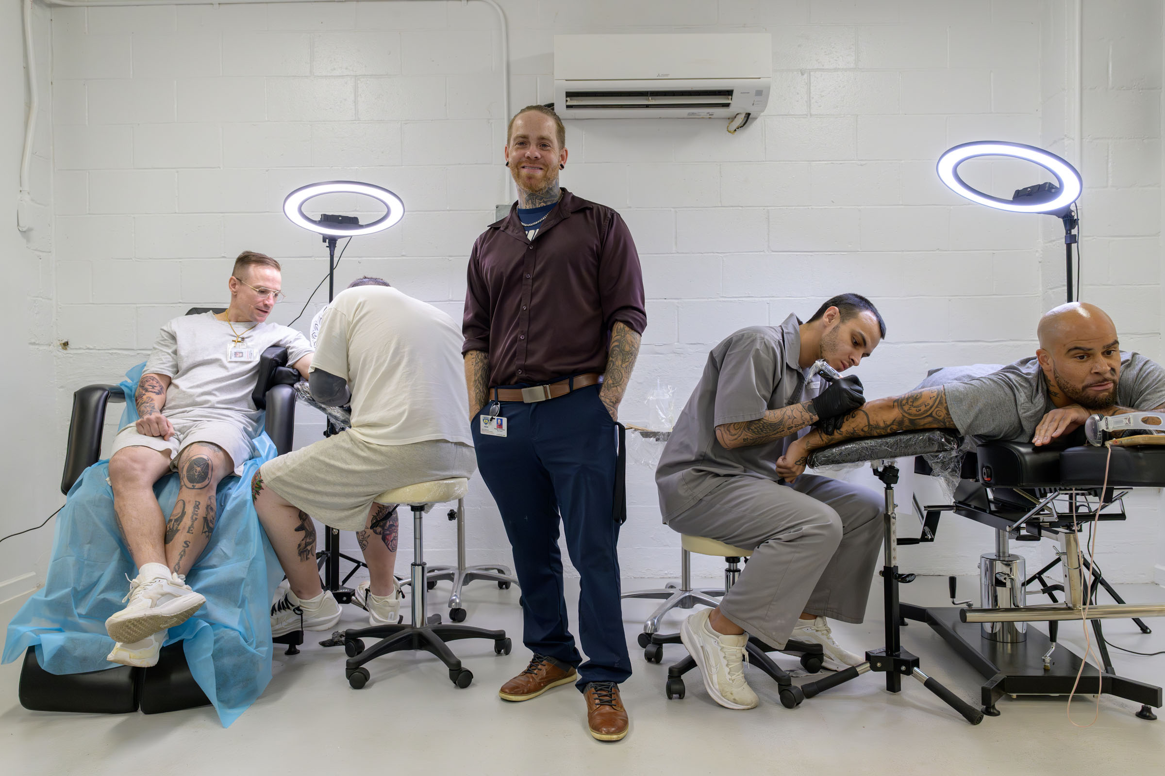 Man stands between tattoo artists working on clients in studio.